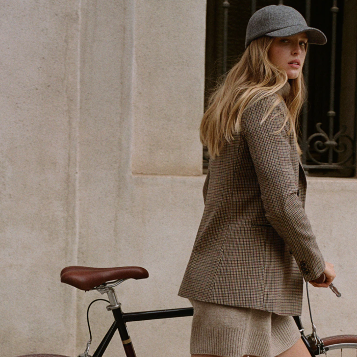 Woman in chic neutral winter outfit and a cap wheeling a bike