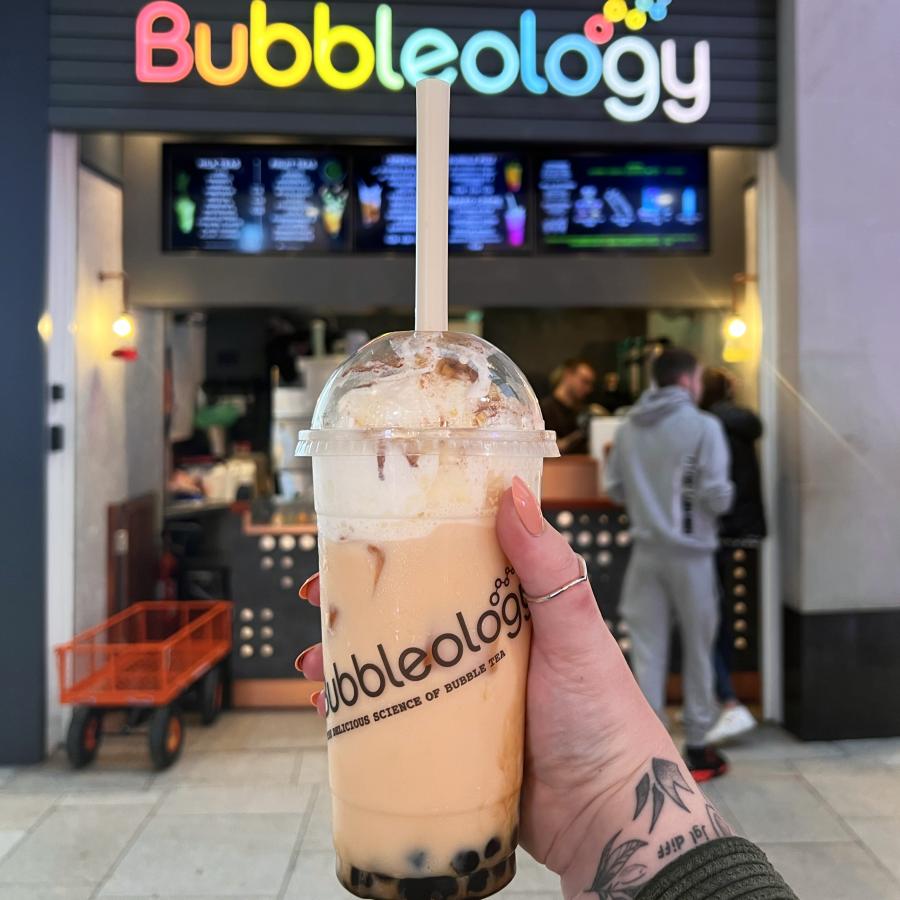 Bubble tea held in front of Bubbleology's rainbow sign